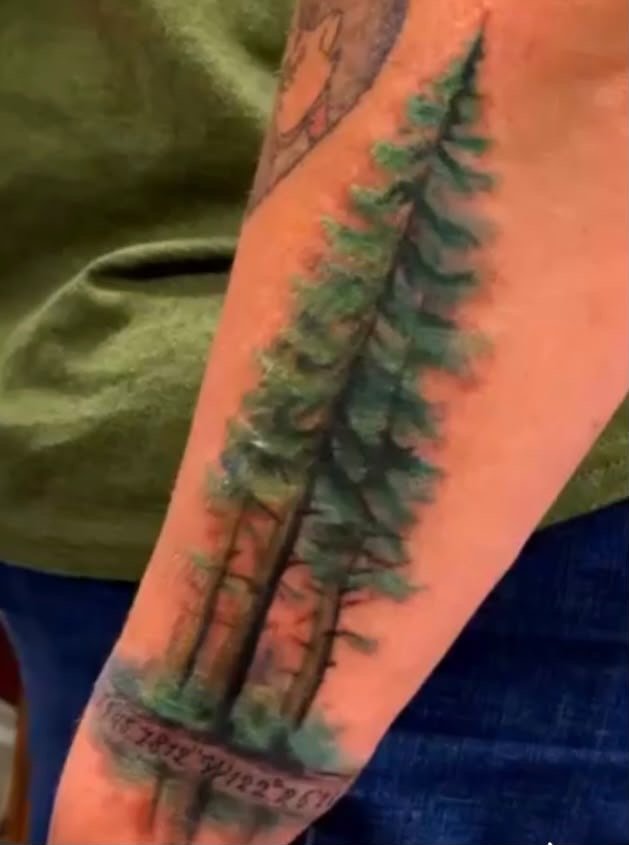 Pine trees forearm tattoo in color realism with GPS coordinates beneath, by Christina